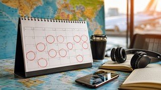 Páginas de um calendário de parede com vários dias circulados em vermelho, sobrepostas a um mapa-múndi desfocado ao fundo, simbolizando o planejamento de uma jornada de aprendizado de idiomas.