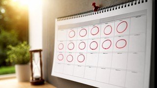 Visão de cima de um calendário de parede com vários dias marcados com um círculo, simbolizando o planejamento e a passagem do tempo para concluir um curso online.