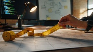 Uma fita métrica amarela com marcações de horas, que se desenrola sobre as páginas de um calendário, passando por vários dias e semanas, simbolizando a conversão do tempo de um curso em um período real.