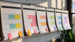 Uma sequência de calendários de parede sobrepostos, com dias marcados em cores diferentes, simbolizando a passagem do tempo e o planejamento de um projeto de estudo a longo prazo.